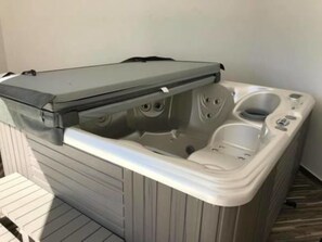 A portable hot tub with a cover, a built-in seat, and a control panel.