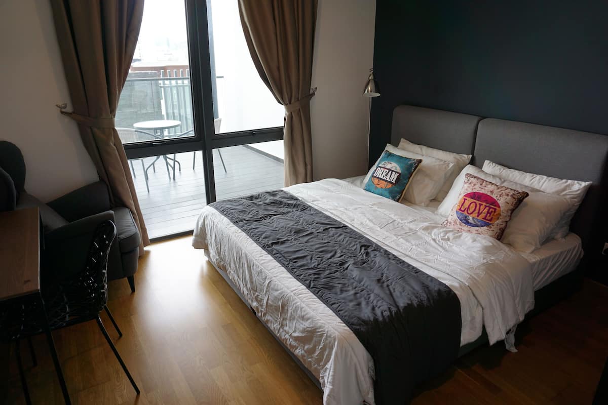 A bedroom with a bed, a desk, and a view of the outside.