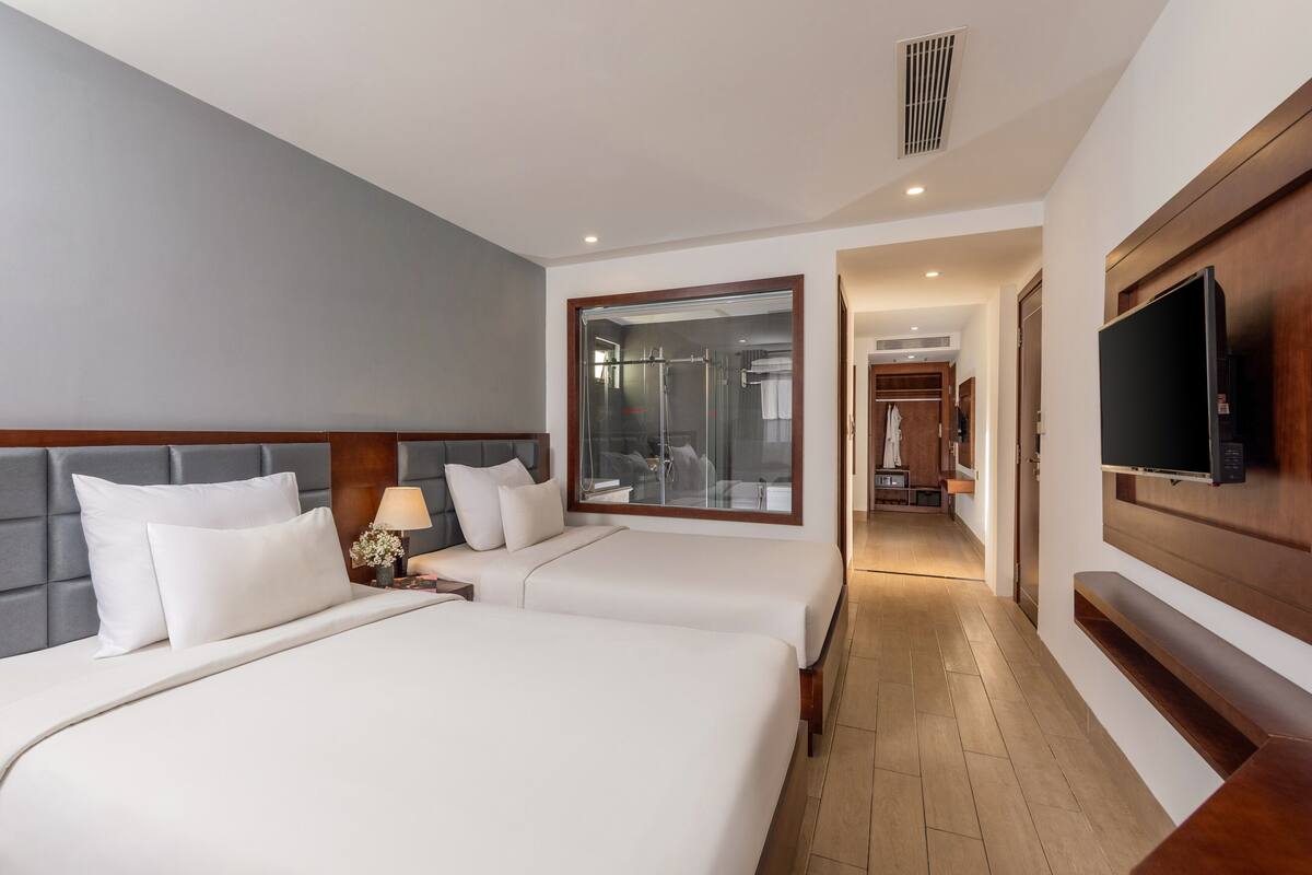 Habitación de hotel con dos camas, televisor, espejo y vestidor.