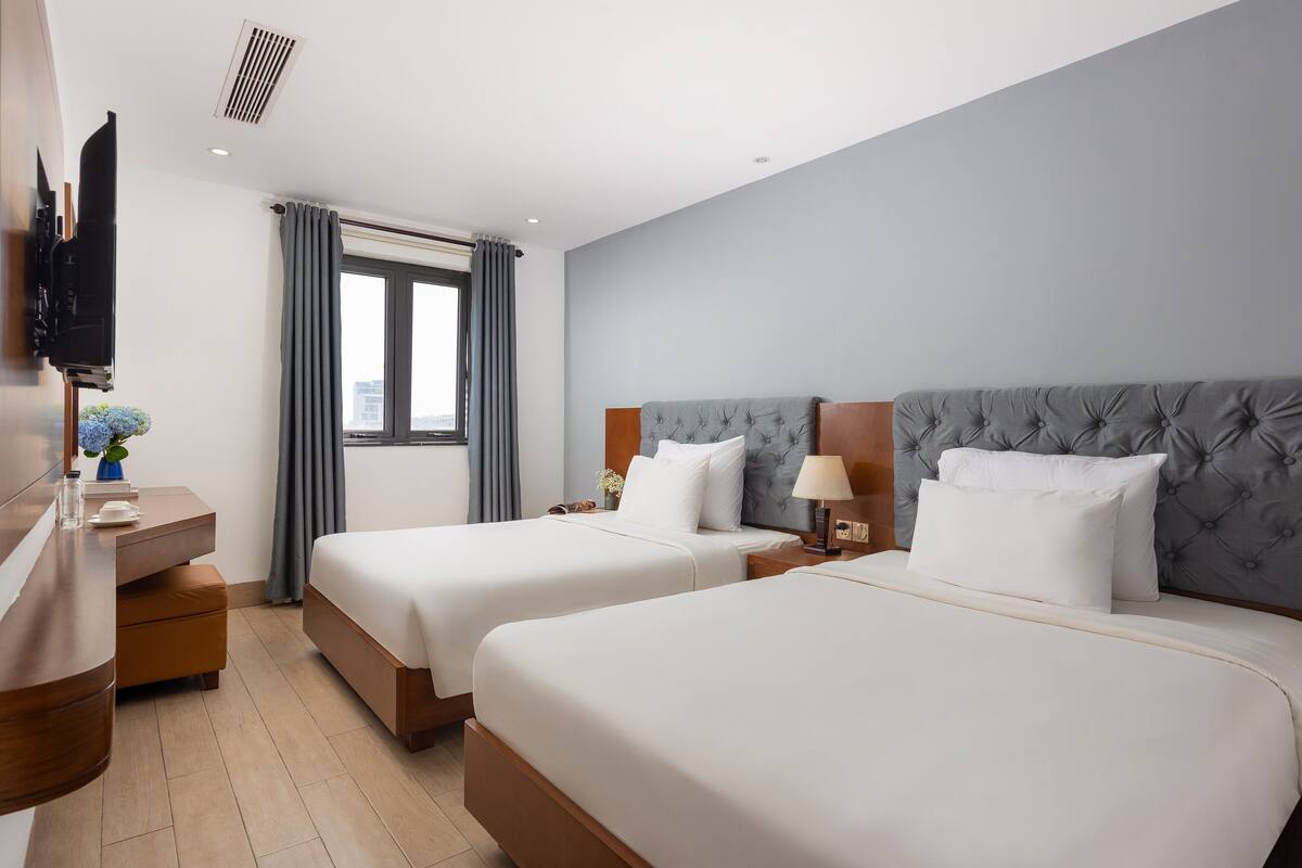 Una habitación de hotel con dos camas, un televisor, un escritorio y una ventana con cortinas.