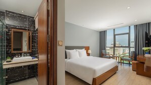 A hotel room with a large bed, a bathroom with a marble vanity, and a city view through large windows. - Sana Danang Beach Hotel (Da Nang)