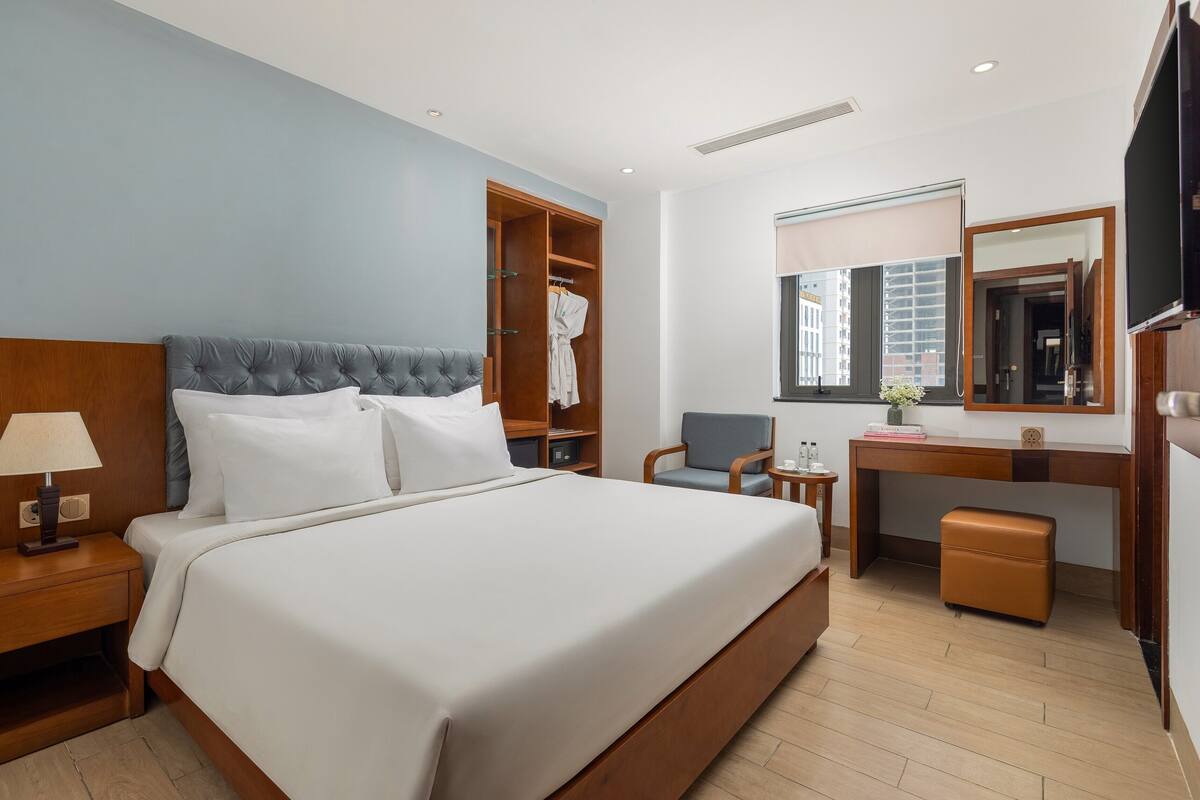 Una habitación de hotel con una cama grande, un escritorio, una silla, un armario y un espejo.