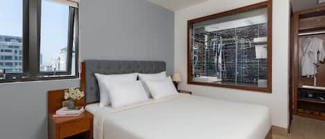 A neatly made bed with white linens, a grey upholstered headboard, and a bedside table with a vase of flowers and books.