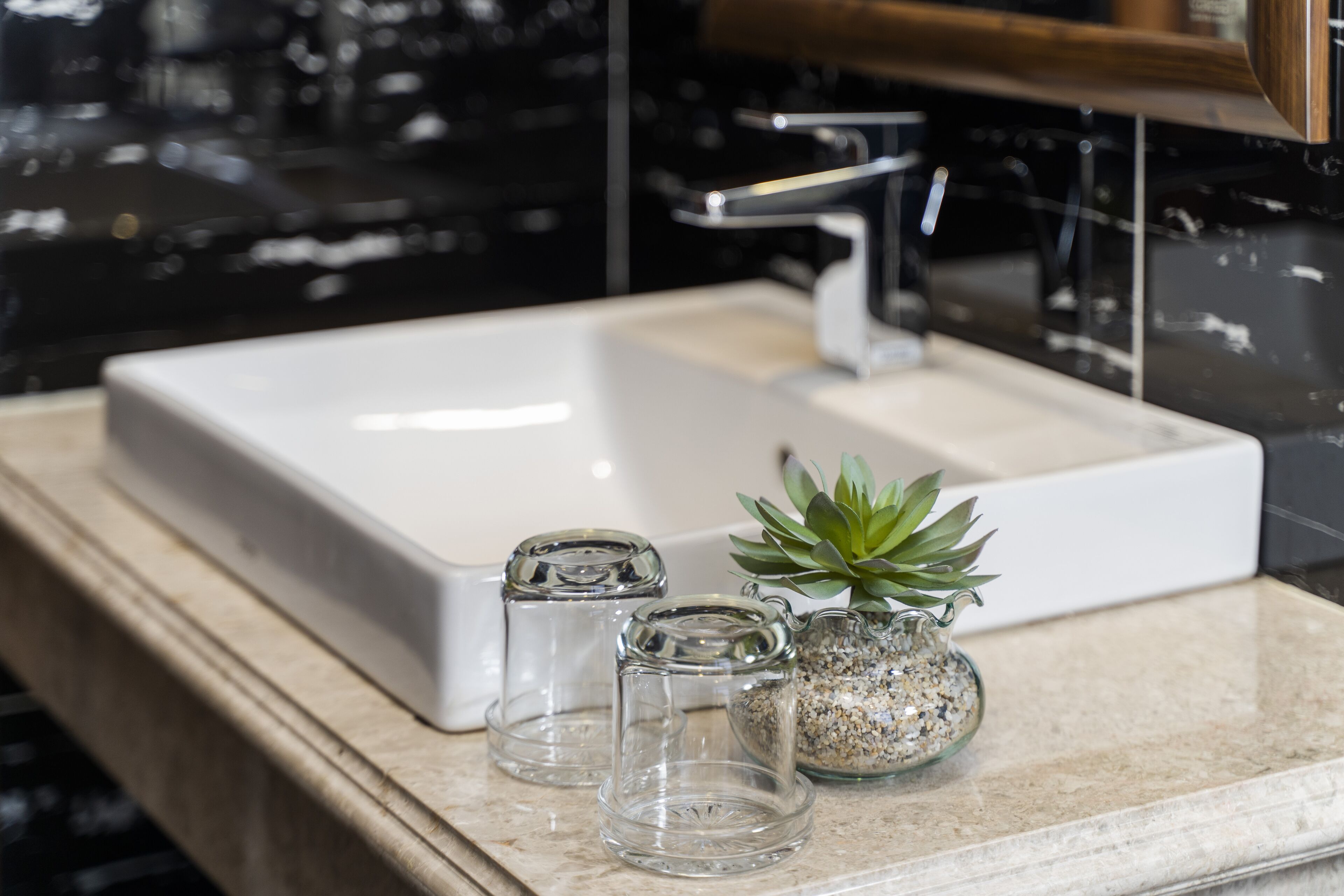Une salle de bain avec un lavabo blanc, un robinet moderne et une petite plante en pot posée sur le comptoir.