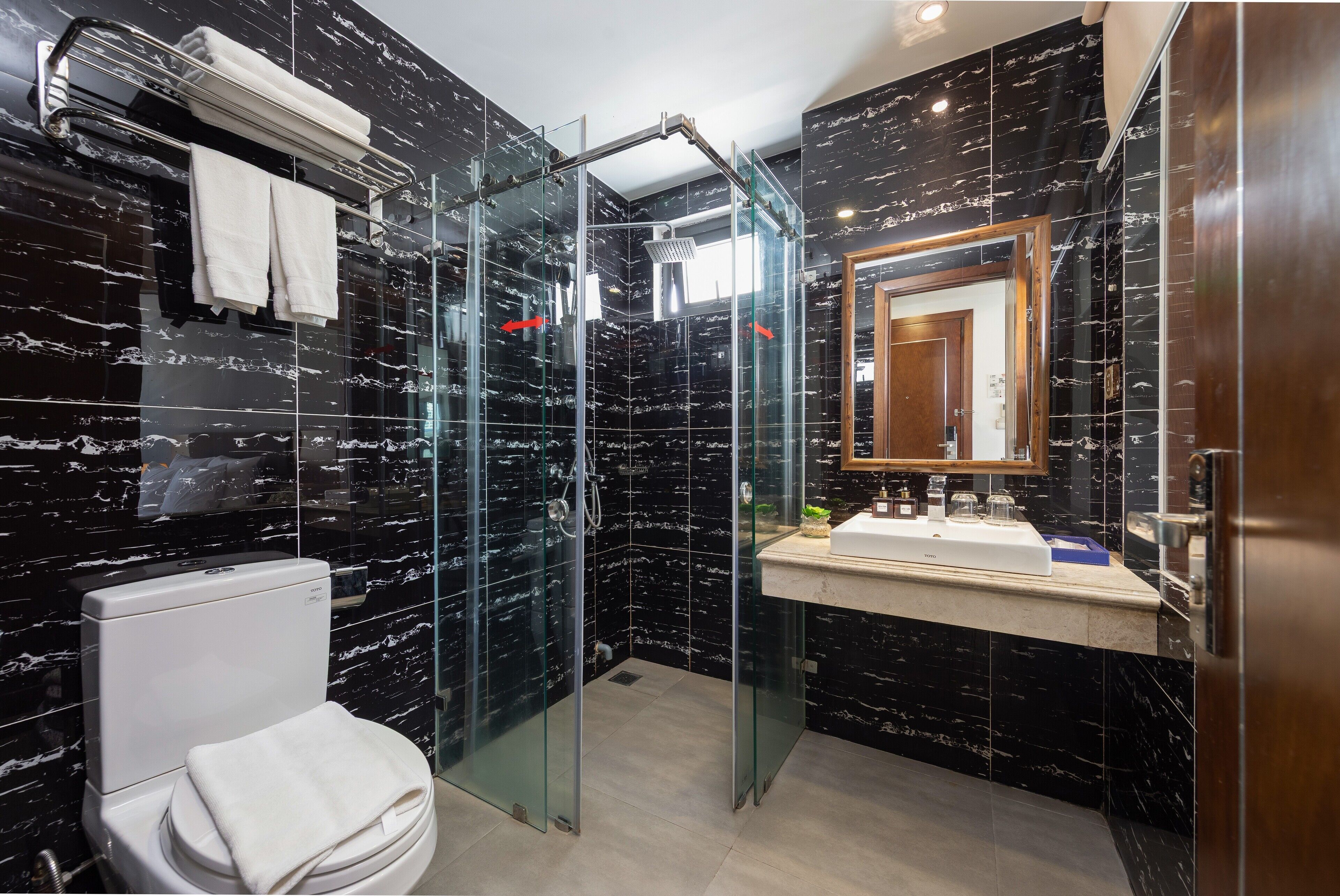 A modern bathroom with a glass-enclosed shower, a white toilet, and a marble-tiled wall.