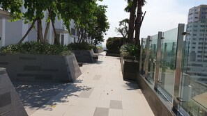 A modern outdoor corridor with tiled flooring, planters with greenery, and a glass railing overlooking a cityscape. - Stay In Vietnam River Gate (Ho Chi Minh City)