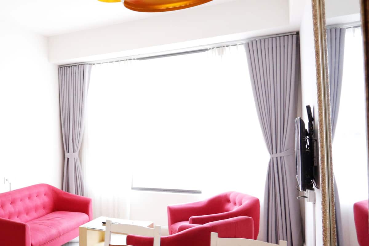 Ein modernes Hotelzimmer mit großem Fenster, einem roten Sofa, einem kleinen Tisch und einer Topfpflanze.