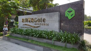 A sign for Rivergate Residence with a modern design, featuring a stone facade and a green logo. - Stay In Vietnam River Gate (Ho Chi Minh City)