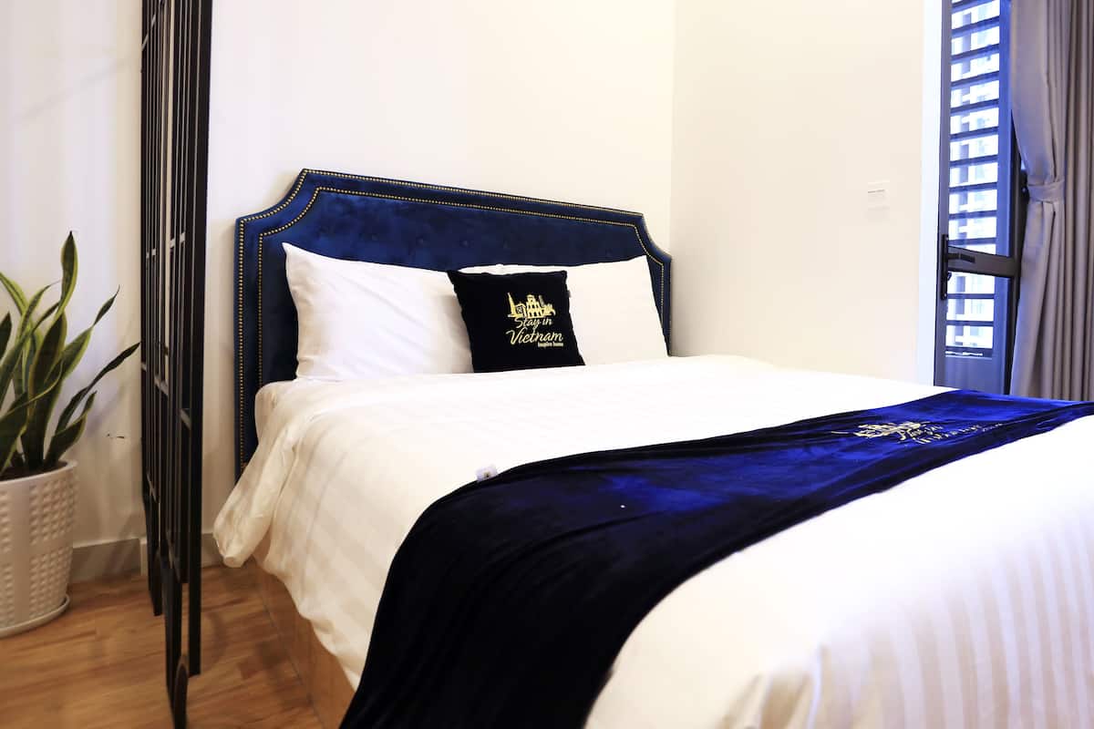 Ein ordentlich bezogenes Bett mit dunkelblauer Kopfteil und einem Kopfkissen mit Hotel-Logo.