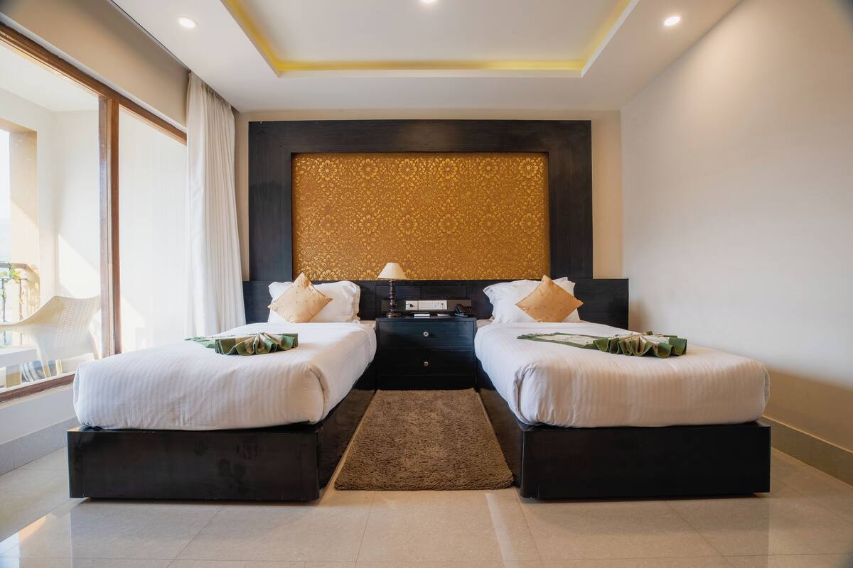 A modern hotel room with two beds, a dark headboard, a decorative wall panel, and a large window.