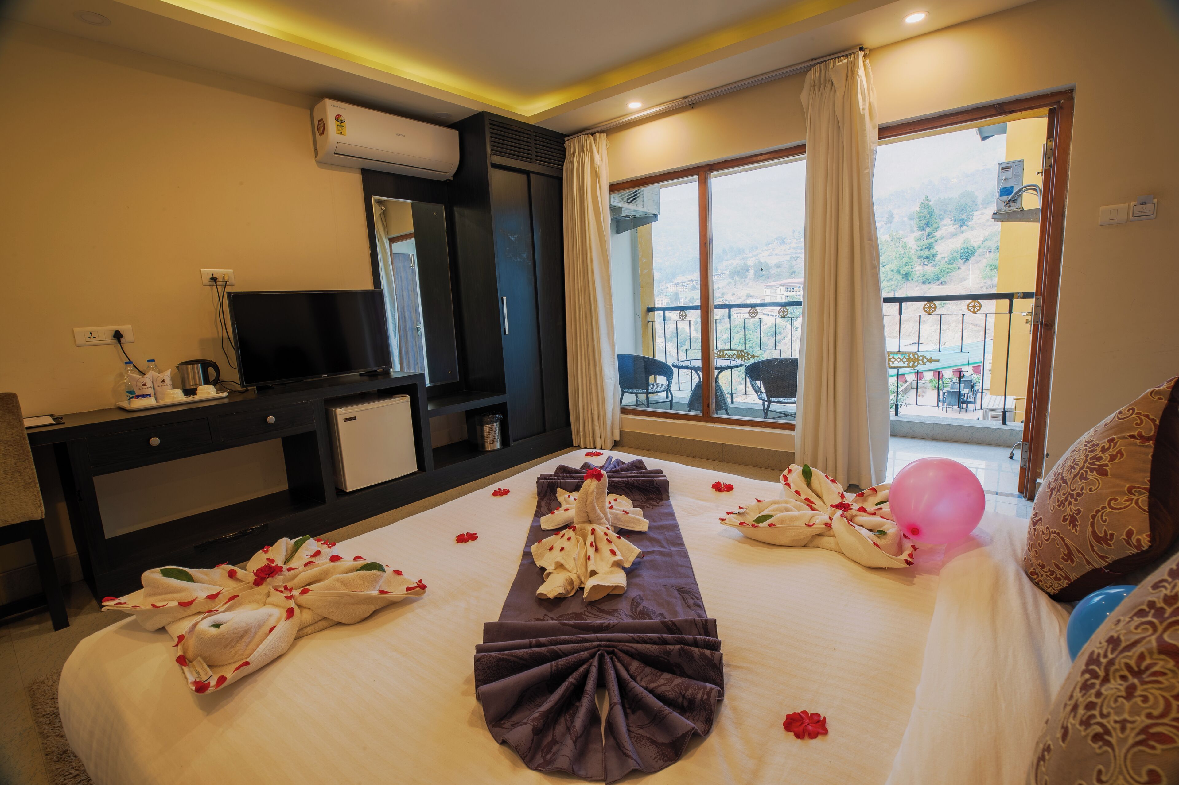 Habitación de hotel con cama, televisión, escritorio, balcón con vistas y ventana con cortinas.