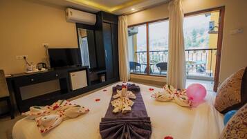 Habitación de hotel con cama, televisión, escritorio, balcón con vistas y ventana con cortinas.