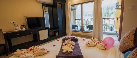A hotel room with a bed, a TV, a desk, a balcony with a view, and a window with curtains.