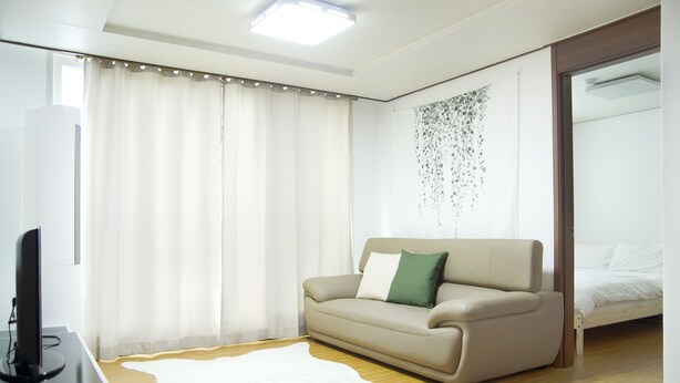 Quarto de hotel moderno com sofá bege, tapete branco e cama com roupa de cama branca.