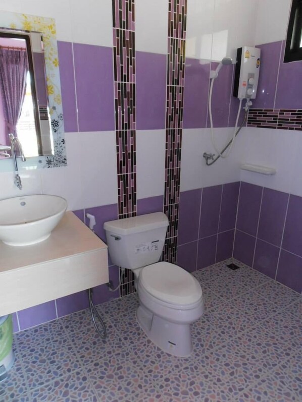 A bathroom with a white sink, toilet, and shower. The walls are tiled in purple and white, and the floor has a mosaic tile pattern.