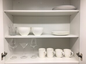 Interior blanco con estantes que contienen cuencos, platos, vasos y tazas blancos.
