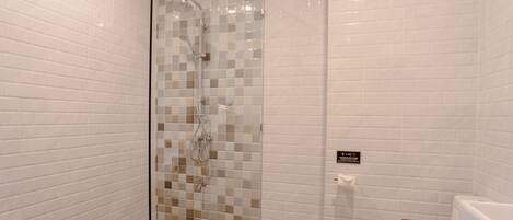 A modern bathroom with a glass-enclosed shower, white tiled walls, and a toilet with a brown vanity.