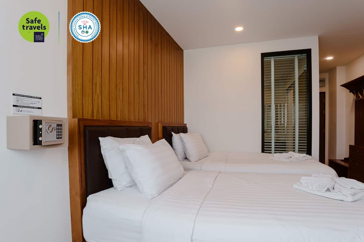 A hotel room with two beds, wooden paneling on the wall, a safe, and a window with blinds.