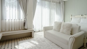Ein Schlafzimmer mit einem Bett, einem weißen Sofa mit flauschigen Kissen, einer Bank und transparenten Vorhängen.