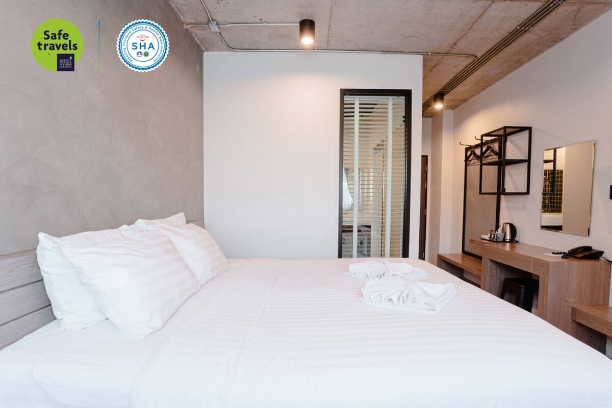 A hotel room with a bed, a desk, a chair, and a mirror.