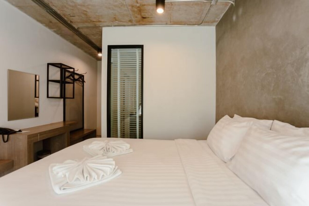 A hotel room with a large bed, a wooden nightstand, a mirror, and a door with blinds.