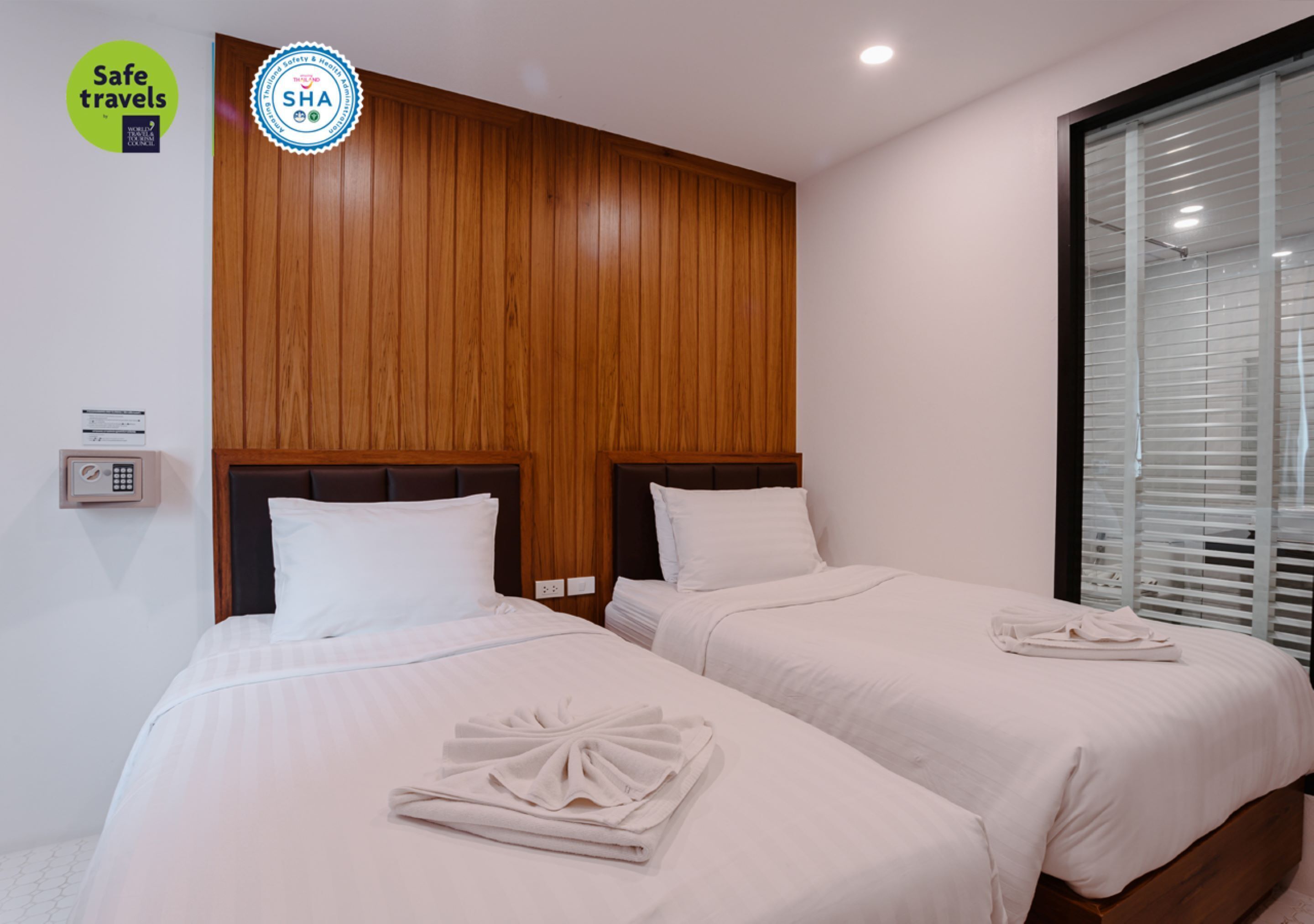 A hotel room with two beds, wooden headboards, white bedding, and a window with blinds.