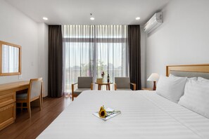 A hotel room with a large bed, a desk, two chairs, a small table with a vase of flowers, and a view through sheer curtains. - Sunflower International Village (Hai Phong)