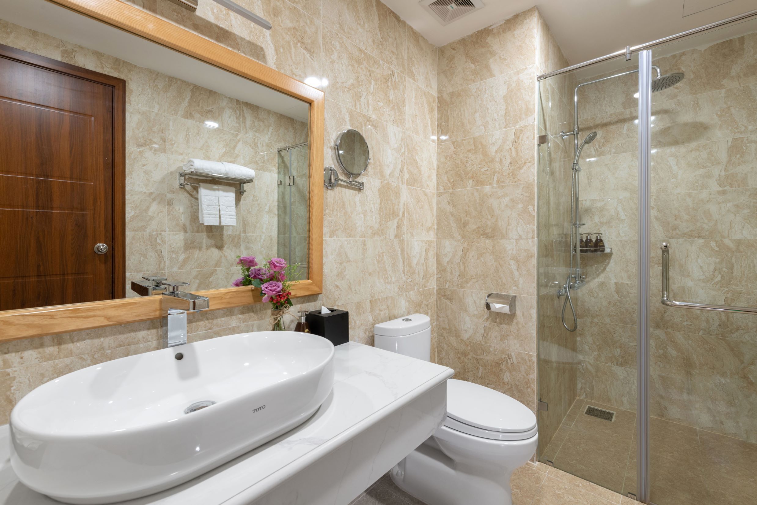 Un baño moderno con un lavamanos ovalado grande, un inodoro y una ducha con mampara de vidrio.