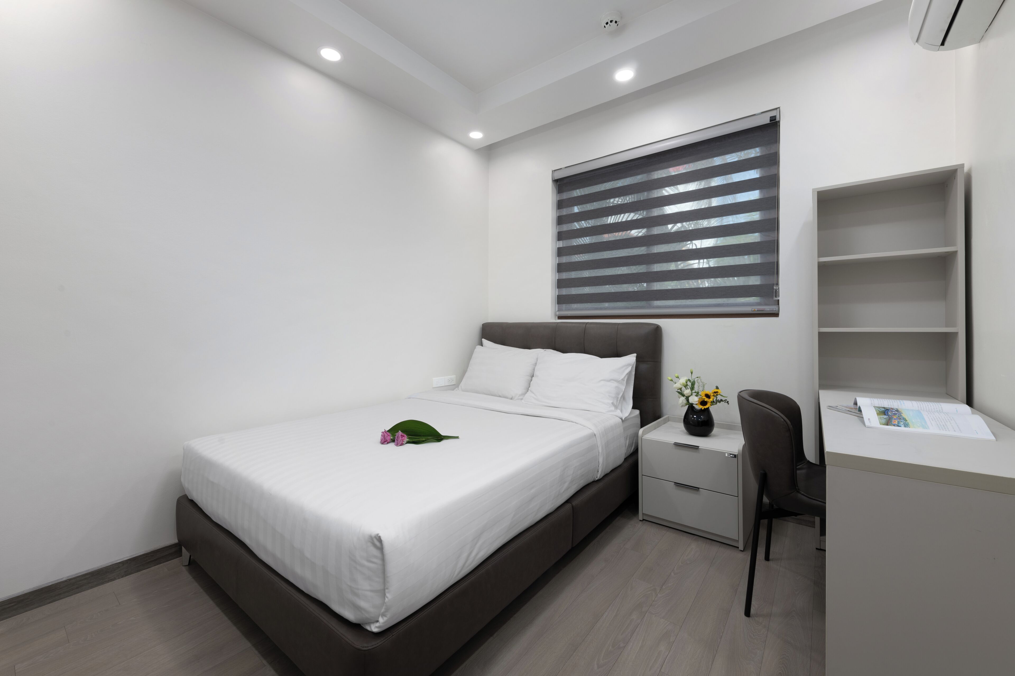 Una camera da letto moderna con un letto, un comodino, una sedia e una scrivania con altra sedia.