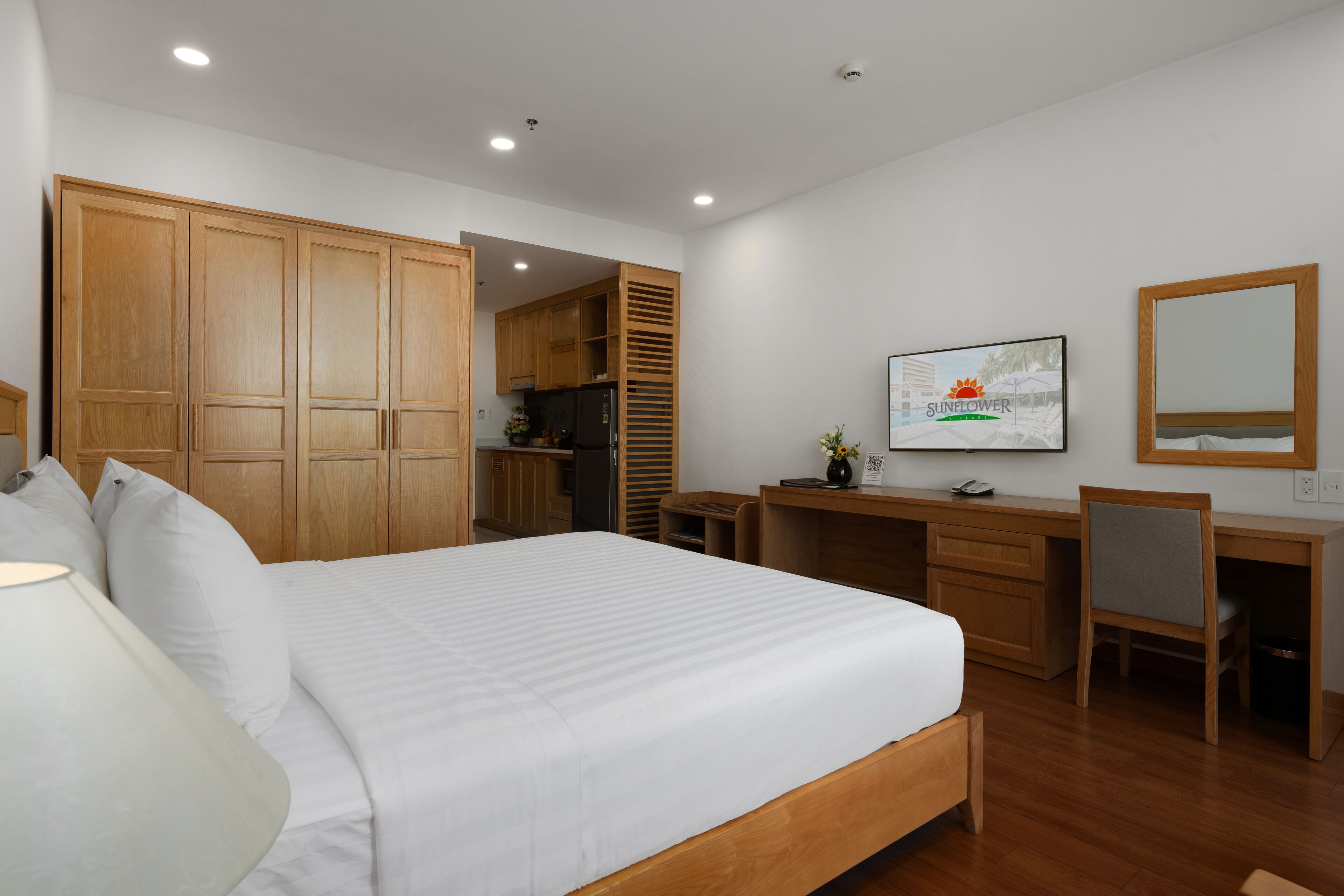 A bedroom with a large bed, wooden wardrobe, desk, chair, and a television.