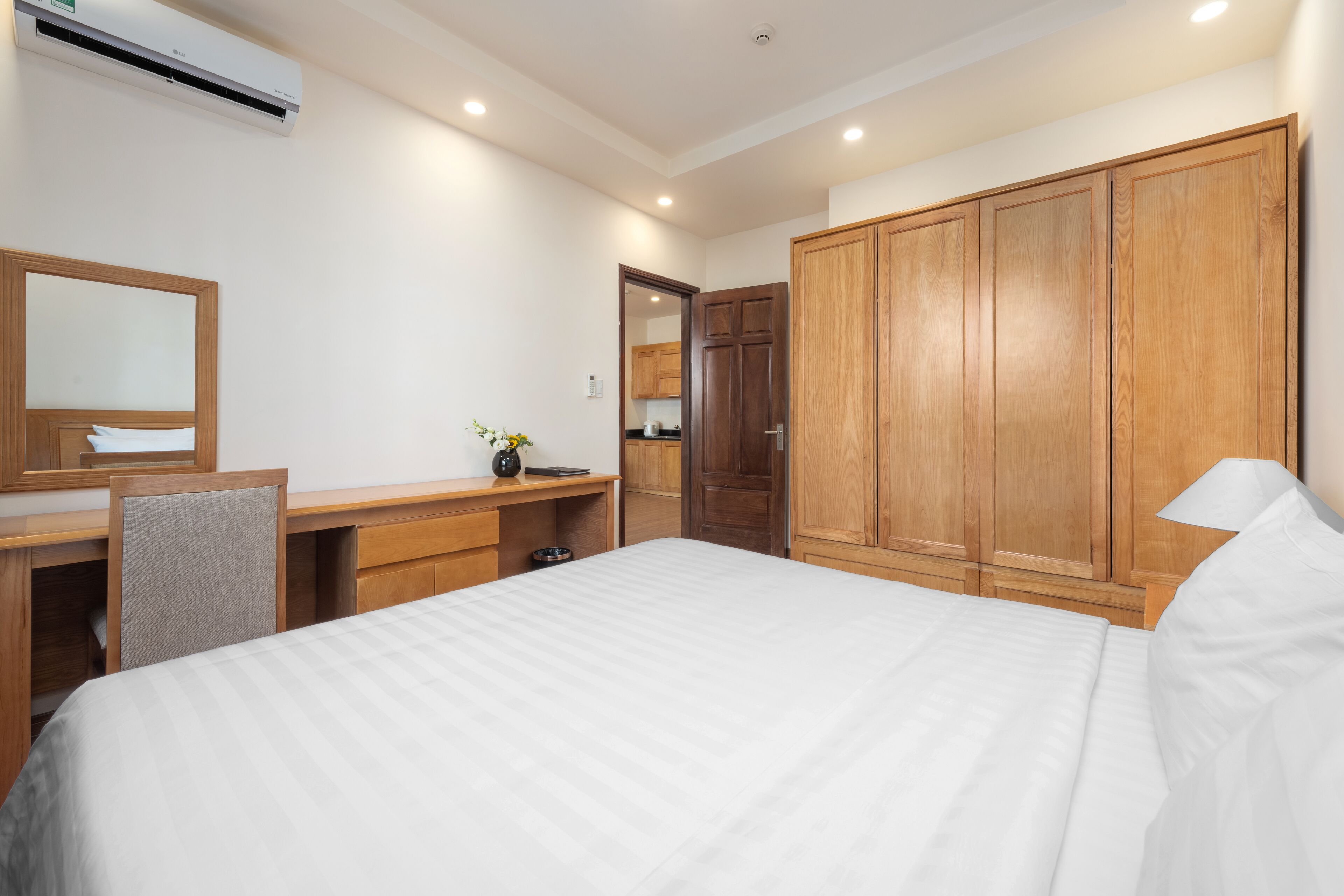 A hotel room with a large bed, wooden wardrobe, desk with chair, and a mirror.