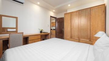 A hotel room with a large bed, wooden wardrobe, desk with chair, and a mirror.