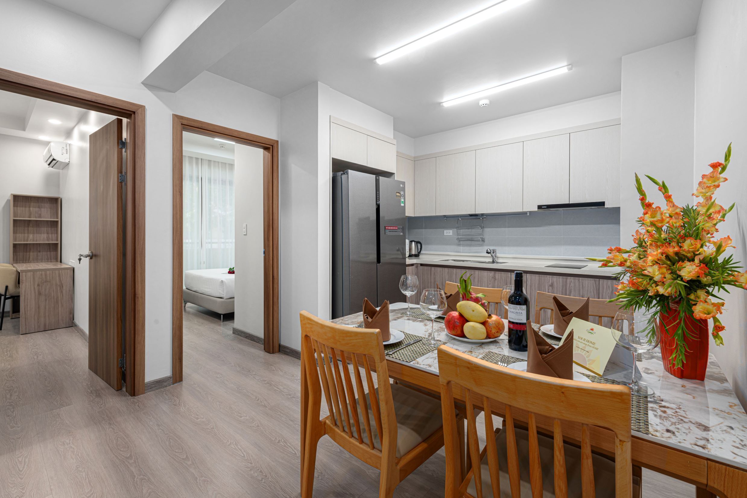 Une cuisine moderne avec des meubles blancs, un réfrigérateur en acier inoxydable et un coin repas avec des chaises en bois et une table dressée pour deux personnes.