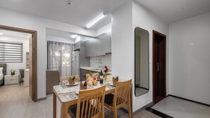 A modern dining area with a wooden table and chairs, a kitchen in the background, and a large mirror on the wall. - Sunflower International Village (Hai Phong)