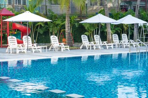 A swimming pool with white lounge chairs and umbrellas, a red slide, and palm trees in the background. - Sunflower International Village (Hai Phong)