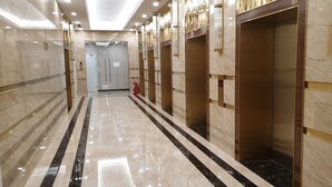 A corridor with marble floors, elevators, and a fire extinguisher.