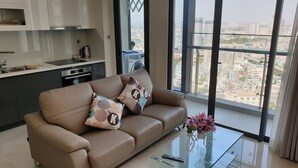 A modern living room with a sofa, a glass coffee table, and a view of a cityscape through large windows.
