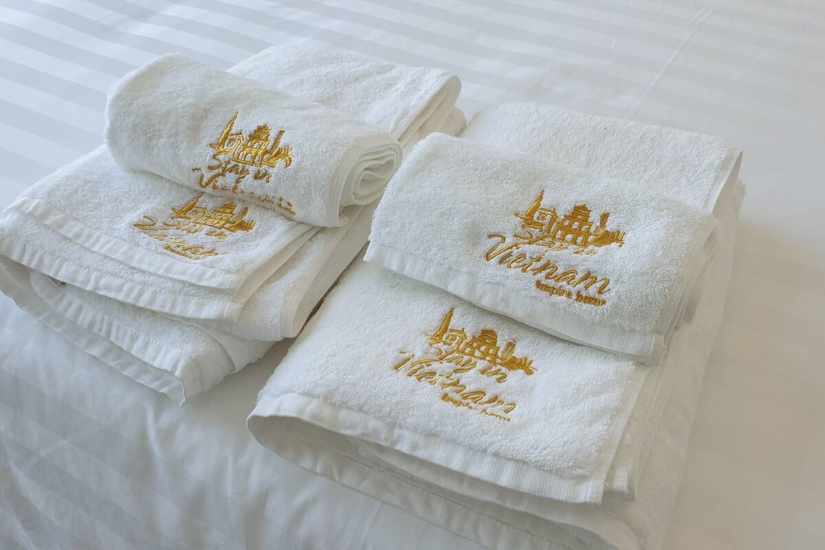 Trois serviettes blanches, soigneusement pliées et ornées de broderies dorées, sont posées sur un lit.