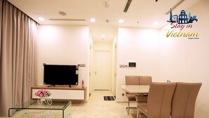 A modern living room with a flat-screen TV, a glass coffee table, a sofa, and a dining area with a table and chairs.