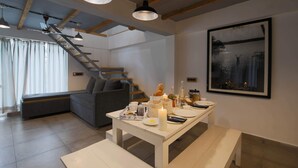 A modern living room with a dining table set for two, a staircase, a grey sofa, and a framed artwork on the wall. - Seclude Kasauli (Kasauli)