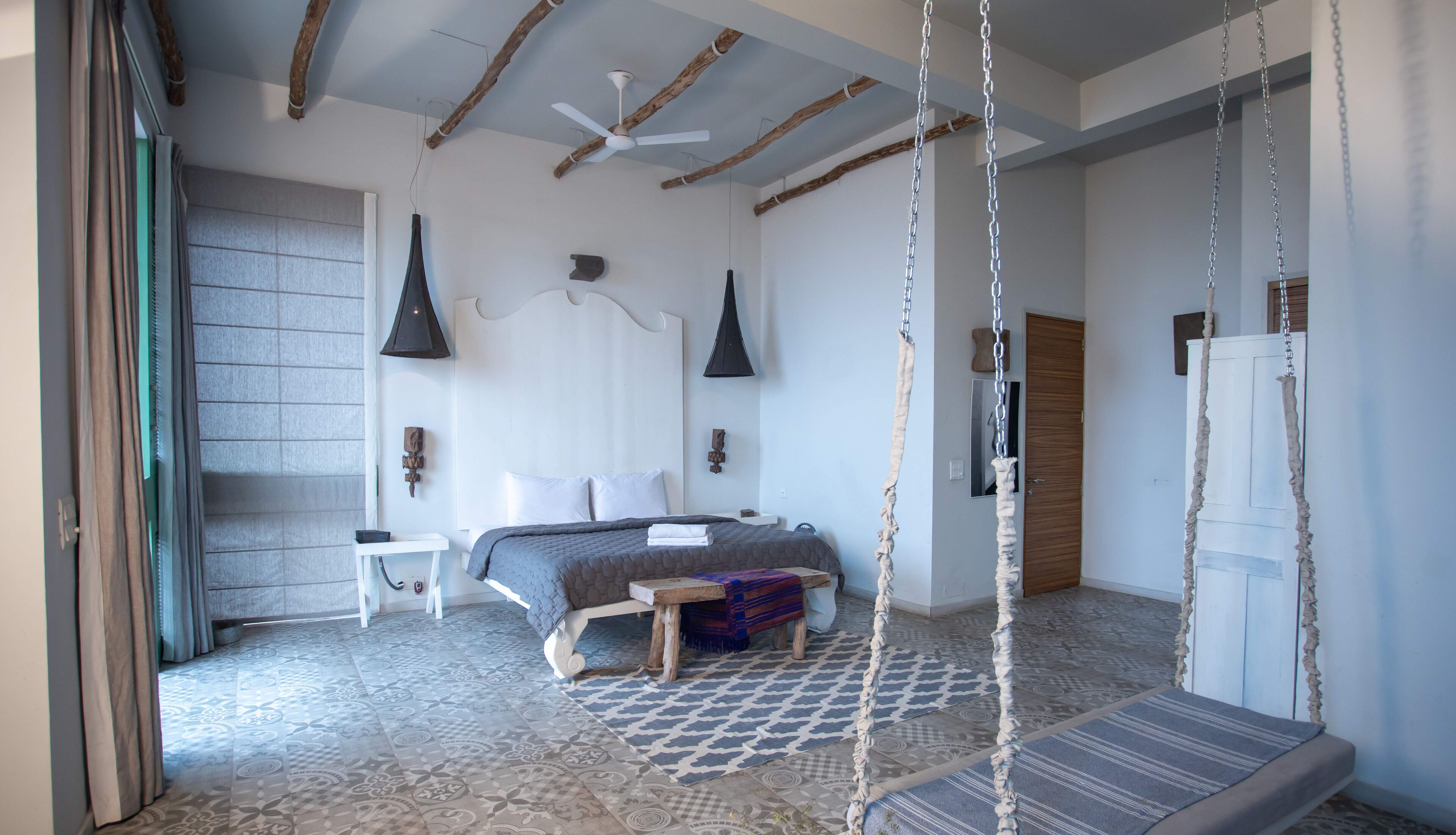 A bedroom with a bed, a hanging chair, a ceiling fan, and a patterned floor.