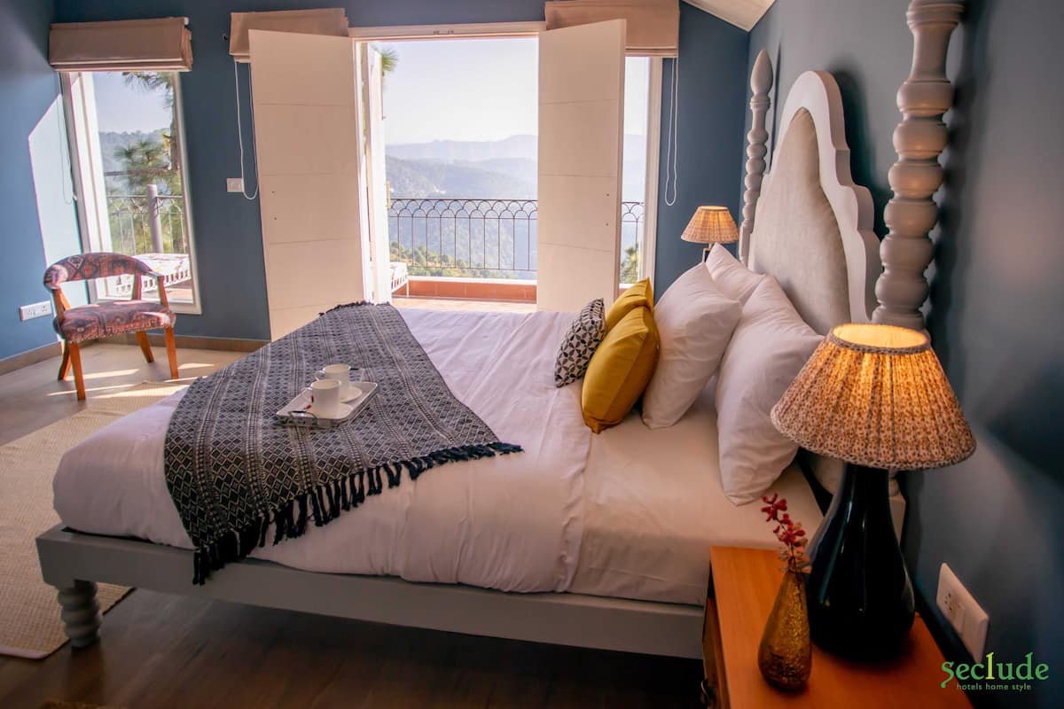Une chambre à coucher comprenant un lit, une chaise, une table de chevet, une lampe et une vue sur l’extérieur.