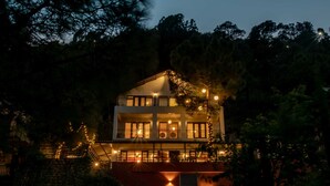 A modern two-story house with a balcony, surrounded by trees and illuminated by string lights. - Seclude Kasauli (Kasauli)