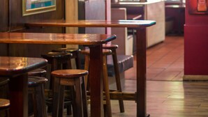 Interior de un restaurante con mesas y taburetes de madera, cuadros en la pared y un cartel que dice 'TAFEL LAGER'.