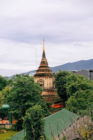 A traditional temple with a tiered roof structure, surrounded by lush greenery and a mountain backdrop. - Jeune Hostel Chiang Mai (Chiang Mai)