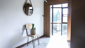 A room with a large window, a round mirror, a wooden chair, and a wicker basket with a plant. - Jeune Hostel Chiang Mai (Chiang Mai)