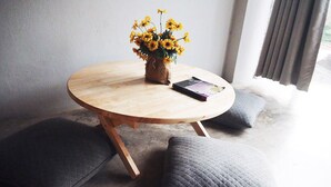 A round wooden table with a vase of yellow flowers and a book, surrounded by two grey cushions. - Jeune Hostel Chiang Mai (Chiang Mai)