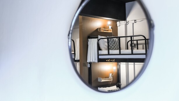 A bunk bed room with a mirror reflecting the interior, a bedside table with a lamp, and a shelf with personal items. - Jeune Hostel Chiang Mai (Chiang Mai)