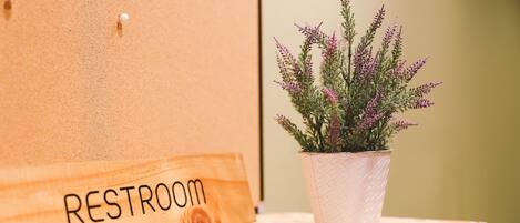 Un letrero de madera con la palabra 'RESTROOM' y una planta en maceta con flores moradas sobre una superficie de madera.