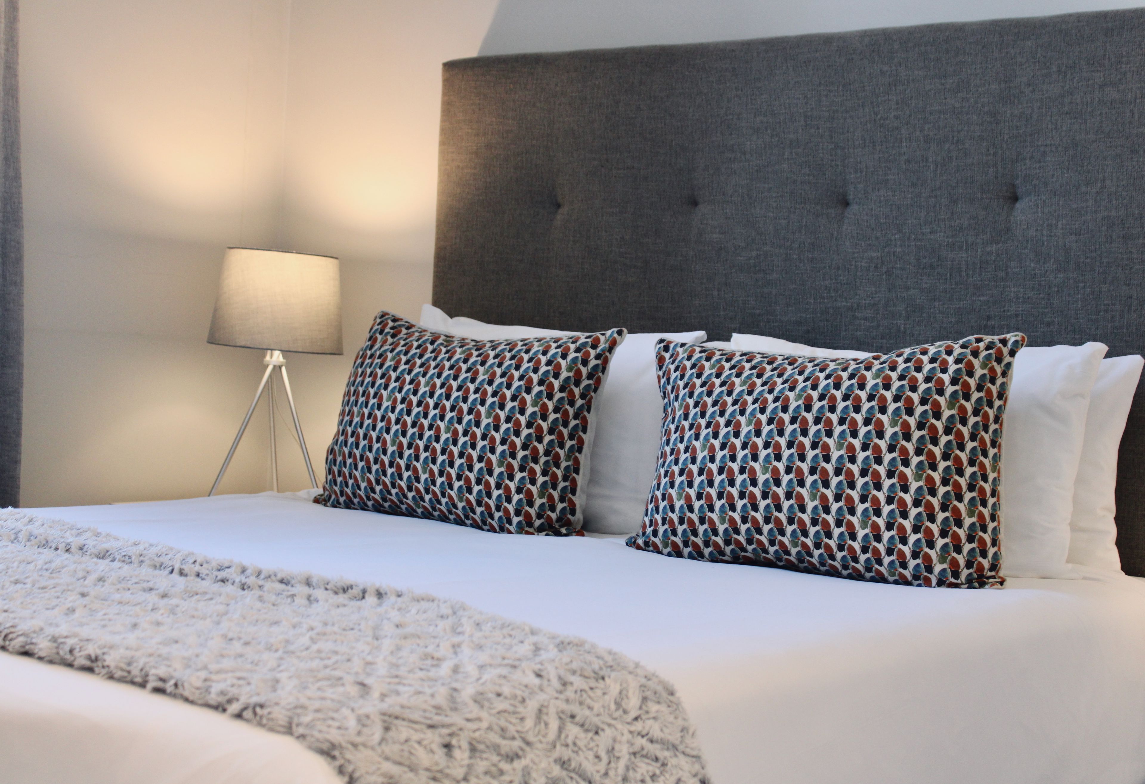 Een hotelkamer met een groot bed, een grijs gestoffeerd hoofdeinde en gekleurde kussens.